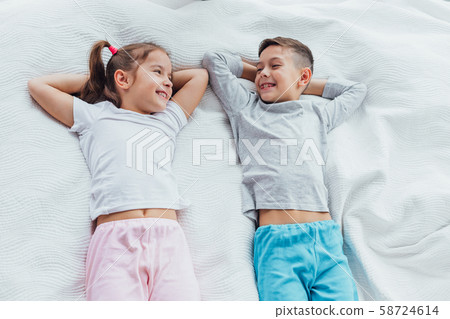 Top view on two beautiful siblings lying on a bed together, smiling while having a rest. 58724614