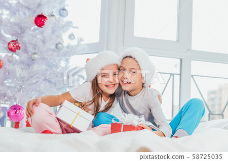 Image of brother and sister in santa hats, tenderly embracing, sharing Christmas presents, sitting Image of brother and sister in santa hats, tenderly embracing, sharing Christmas presents, sitting 58725035