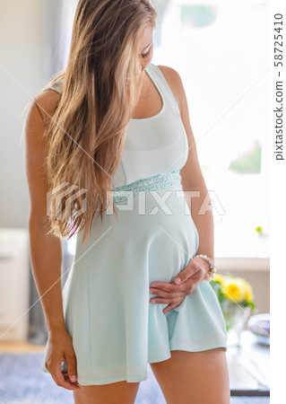 Smiling pregnant woman standing with her hands at belly Smiling pregnant woman standing with her hands at belly 58725410