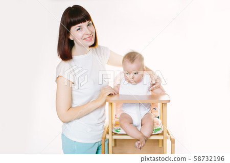 Young beautiful mother puts a white bib on her baby girl, sitting at a chair. Young beautiful mother puts a white bib on her baby girl, sitting at a chair. 58732196