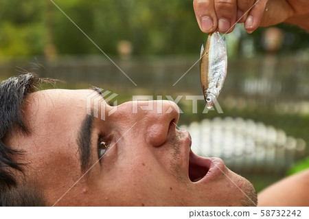 Holding a very small fish above open mouth Holding a very small fish above open mouth 58732242
