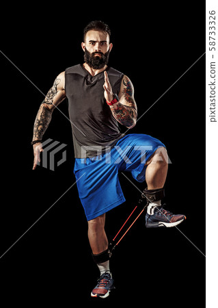 Young athlete squatting exercise with resistance band around legs. Full body length over black Young athlete squatting exercise with resistance band around legs. Full body length over black 58733326