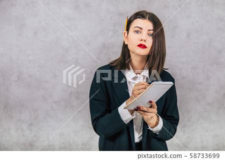 Cute concentrated business women standing with pencil behind her ear and listening, writing down Cute concentrated business women standing with pencil behind her ear and listening, writing down 58733699