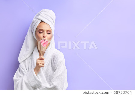 Young woman in towel and bathrobe with lollipop isolated over purple background Young woman in towel and bathrobe with lollipop isolated over purple background 58733764