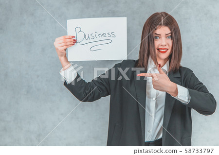 Inspired businesswoman in black suit showing sheet of paper with word business , pointing her finger 58733797