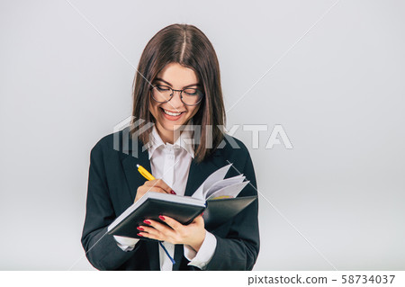 Pretty young businesslady in black suit standing, listening attentively, noting something in her Pretty young businesslady in black suit standing, listening attentively, noting something in her 58734037