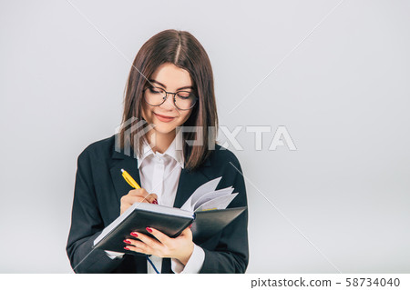 Pretty young businesslady in black suit standing, listening attentively, noting something in her Pretty young businesslady in black suit standing, listening attentively, noting something in her 58734040