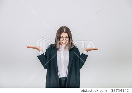 Pretty young businesswoman in black suit standing, throwing her hands with opened palms for text or 58734142