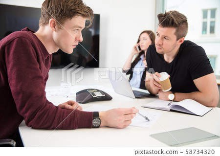 Businessmen Discussing While Colleague Using Smart Phone 58734320
