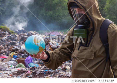 A man in a gas mask looks at the once beautiful planet earth. On the background of burning plastic trash. The concept of environmental problems — plastic garbage, illegal dumps, waste incineration A man in a gas mask looks at the once beautiful planet earth. On the background of burning plastic trash. The concept of environmental problems — plastic garbage, illegal dumps, waste incineration 58734836
