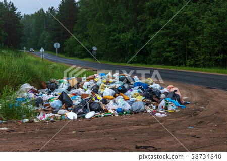Illegal garbage dump at the intersection of a dirt road and highway. Summer residents go to the city from the village and throw trash along the road Illegal garbage dump at the intersection of a dirt road and highway. Summer residents go to the city from the village and throw trash along the road 58734840