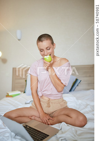 Portrait of cute woman with green apple and laptop in bright bedroom 58740981