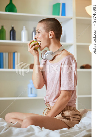Beautiful caucasian girl sits in white bed early in morning, eats green apple Beautiful caucasian girl sits in white bed early in morning, eats green apple 58740983