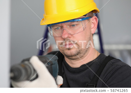 Male adult worker in yellow helmrt hol electric drill in hand. Male adult worker in yellow helmrt hol electric drill in hand. 58741265
