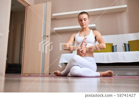 Portrait of attractive young sporty woman wearing white clothing doing yoga exercise in room Portrait of attractive young sporty woman wearing white clothing doing yoga exercise in room 58741427