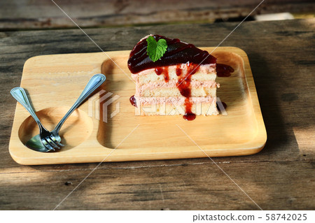 Velvet cake with strawberry smoothie and red syrup, Sweet food with spoon and fork on a wooden plate with brown table in background 58742025