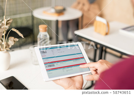 Young man scrolling through electronic document while sitting by table 58743651