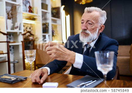 Portrait senior man grey haired sit in restaurant looking electronic cigarette Portrait senior man grey haired sit in restaurant looking electronic cigarette 58745849