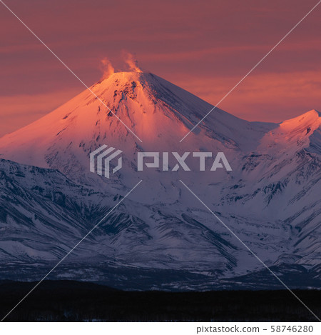 Winter volcanic landscape of Kamchatka Peninsula at purple-violet sunset: active volcano erupting Winter volcanic landscape of Kamchatka Peninsula at purple-violet sunset: active volcano erupting 58746280