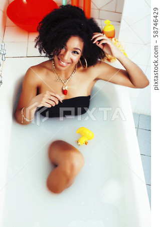 young afro-american teen girl laying in bath with foam, wearing swag jewelry flawless, making selfie 58746429