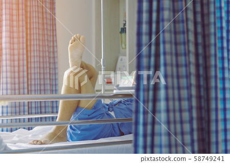 Elderly male patient relaxing on bed with his legs crossed in a good mood to wait for the time to go home. Selective focus on foot sole. Elderly male patient relaxing on bed with his legs crossed in a good mood to wait for the time to go home. Selective focus on foot sole. 58749241