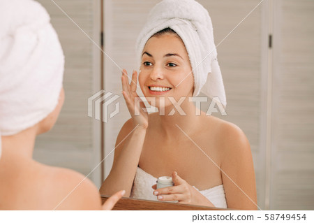 woman applying cream on her face in bathroom 58749454