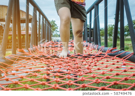 Young woman tried to walk on the bridge floor tied with a red rope to cross the swamp in the fields. Selective focus on her leg. 58749476