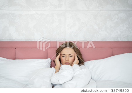 Low-spirited young woman with headache lying in bed 58749800
