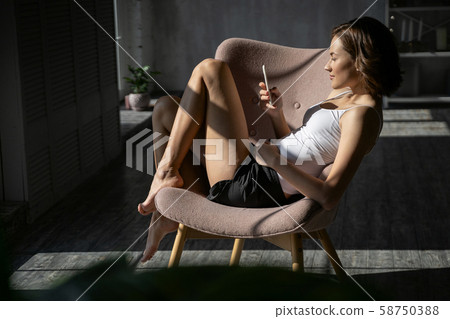 Woman in an armchair using her smartphone Woman in an armchair using her smartphone 58750388