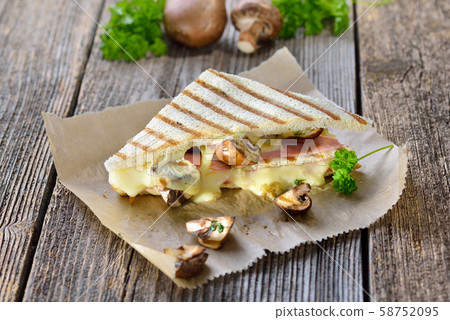 Pressed and toasted double panini with ham, cheese and mushrooms served on sandwich paper Pressed and toasted double panini with ham, cheese and mushrooms served on sandwich paper 58752095