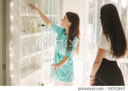 Female cosmetologis show to client cosmetology product. Doctor recommends different serum and face Female cosmetologis show to client cosmetology product. Doctor recommends different serum and face 58752643