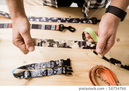 Overview of hands of craftsman holding one of creative pet collar workpieces 58754768