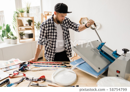 Young creative man printing or sticking decor on one of pet collar workpieces 58754799