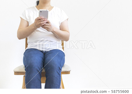 一個小胖女人坐在椅子上,操作智能手機 一個小胖女人坐在椅子上,操作智能手機 58755600
