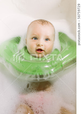 The baby is newborn, the girl is bathing in the bathroom with a inflatable circle around her neck. 58759729
