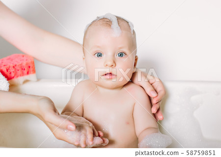 Happy laughing baby taking a bath playing with foam bubbles. Little child in a bathtub. Infant 58759851