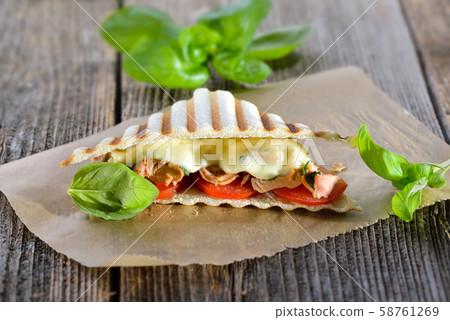 Toasted panini with tuna fish, tomatoes, melted mozzarella and fresh basil served on sandwich paper  58761269