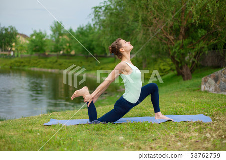 A young sports girl practices yoga on a green lawn 58762759