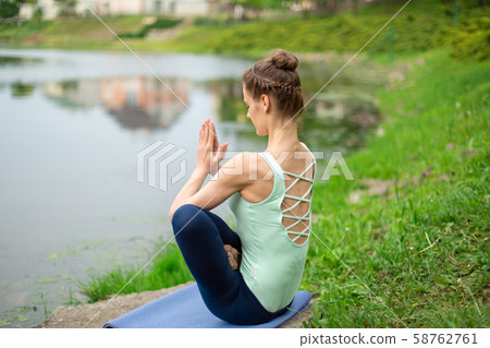 A young sports girl practices yoga on a green lawn A young sports girl practices yoga on a green lawn 58762761