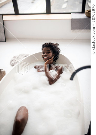 Curly dark-skinned woman smiling broadly while having bath 58762970