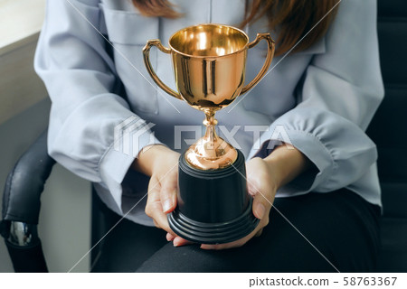 Gold trophy on businesswomen 's hands, successful 58763367