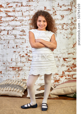 Young joyful girl smiling shyly over a brick wall crossed her arms relaxed 58764109
