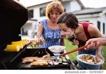 Portrait of multigeneration family outdoors on garden barbecue, grilling. 58765607