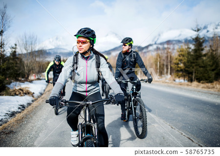 Group of mountain bikers riding on road outdoors in winter. Group of mountain bikers riding on road outdoors in winter. 58765735