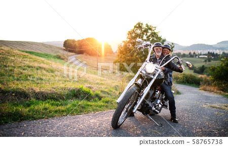 A cheerful senior couple travellers with motorbike in countryside. 58765738