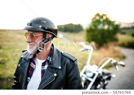 A cheerful senior man traveller with motorbike in countryside, walking. 58765769