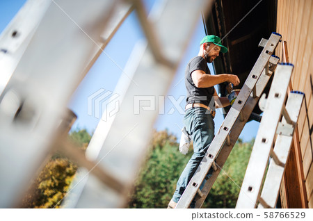 A side view of mature man outdoors in summer, painting wooden house. 58766529