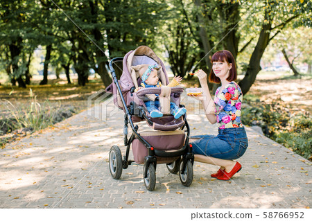 Mom feeding her baby girl with a spoon. Mother giving food to ten-month child walking with baby 58766952