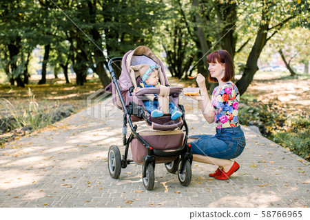 Mom feeding her baby girl with a spoon. Mother giving food to ten-month child walking with baby Mom feeding her baby girl with a spoon. Mother giving food to ten-month child walking with baby 58766965