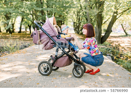 Young mother looking at her child in a baby stroller Young mother looking at her child in a baby stroller 58766990
